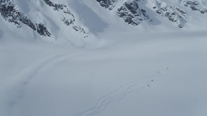 A group of snowmobiles drive across a snowy mountain landscape