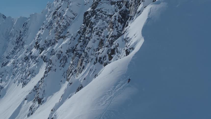 Aerial view of a person climbing a mountain face with layers of snow