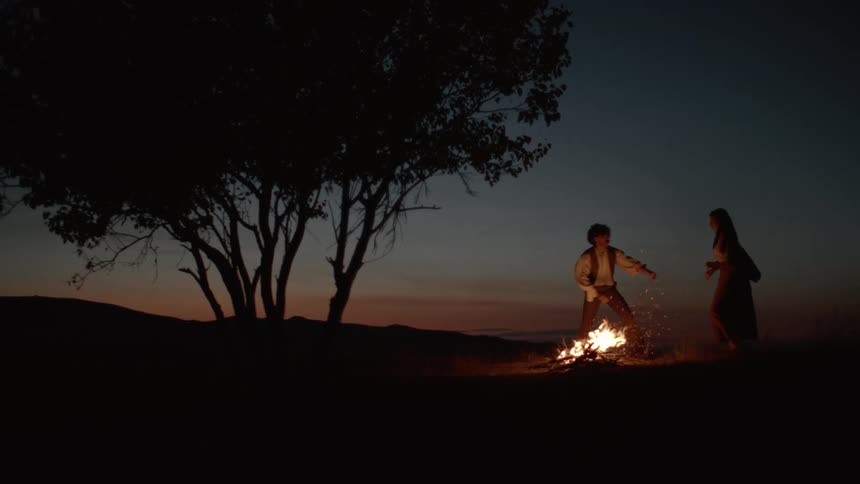 Man and woman hugging next to a campfire at night