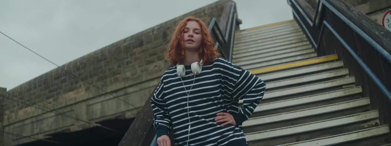 Redhead woman on stairs in an outdoor setting placing her hand on her waist