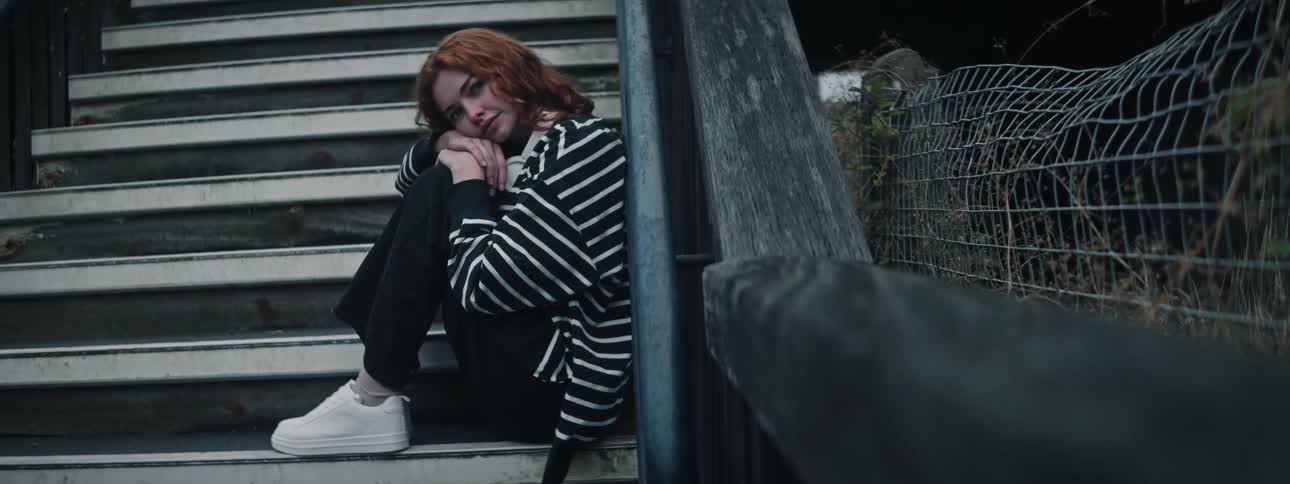A red haired girl sits on a staircase and blinks