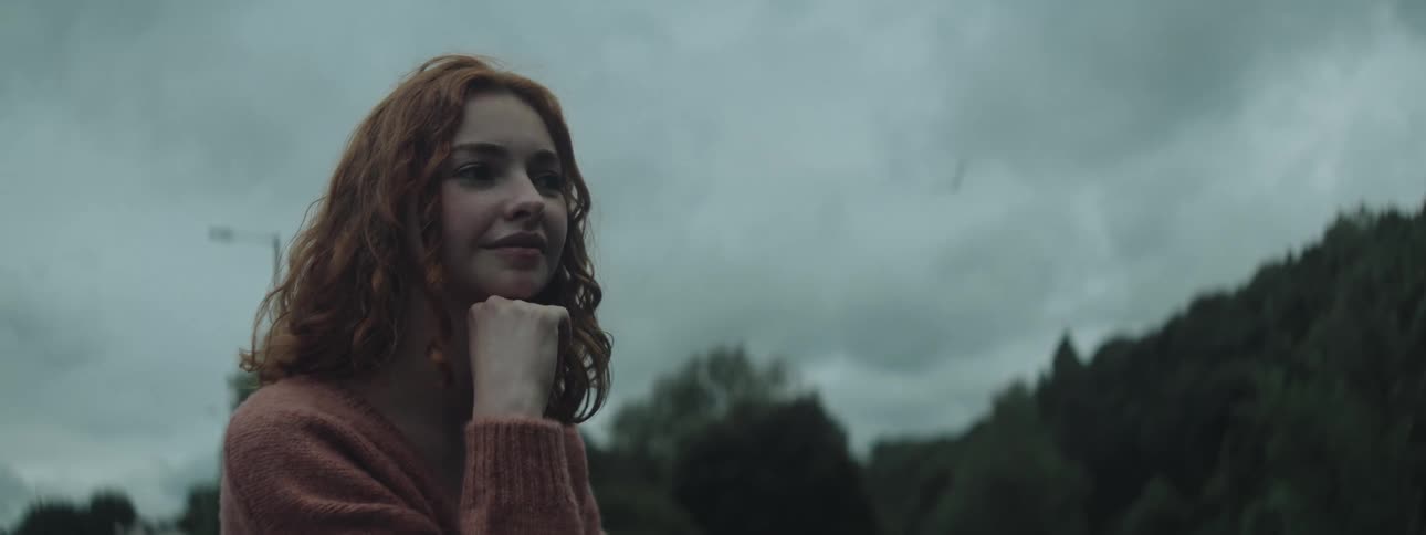 A young woman with red hair thoughtfully gazes into the distance