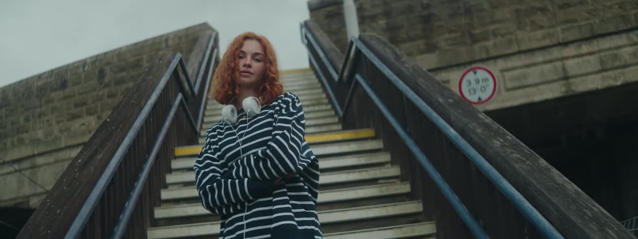 A young woman with red hair stands on staircase modeling for the camera