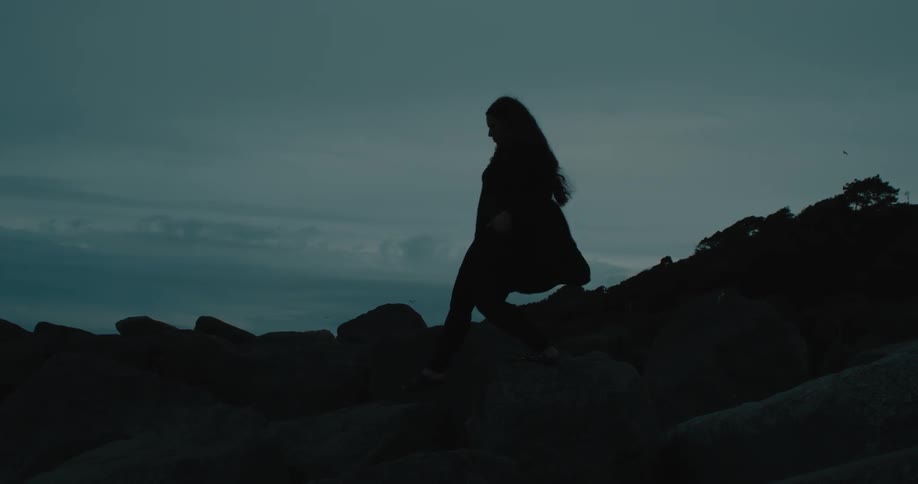 Silhouette of a woman walking among rocks on a dark dawn