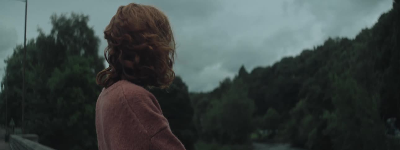 A woman with orange hair who is moving because of the wind is standing looking forward