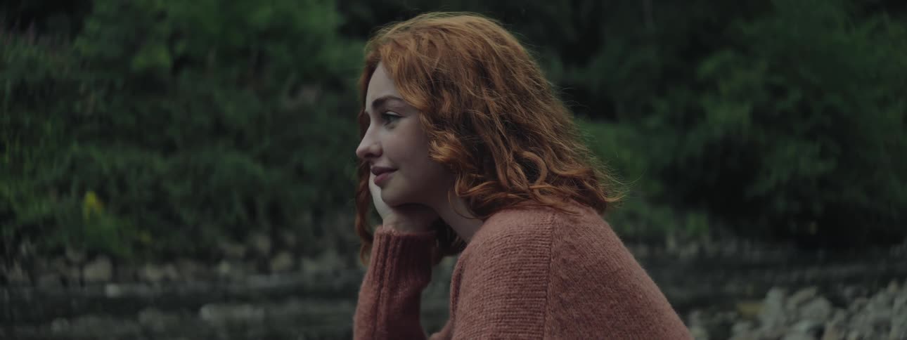 Smiling redheaded woman sits by a stream