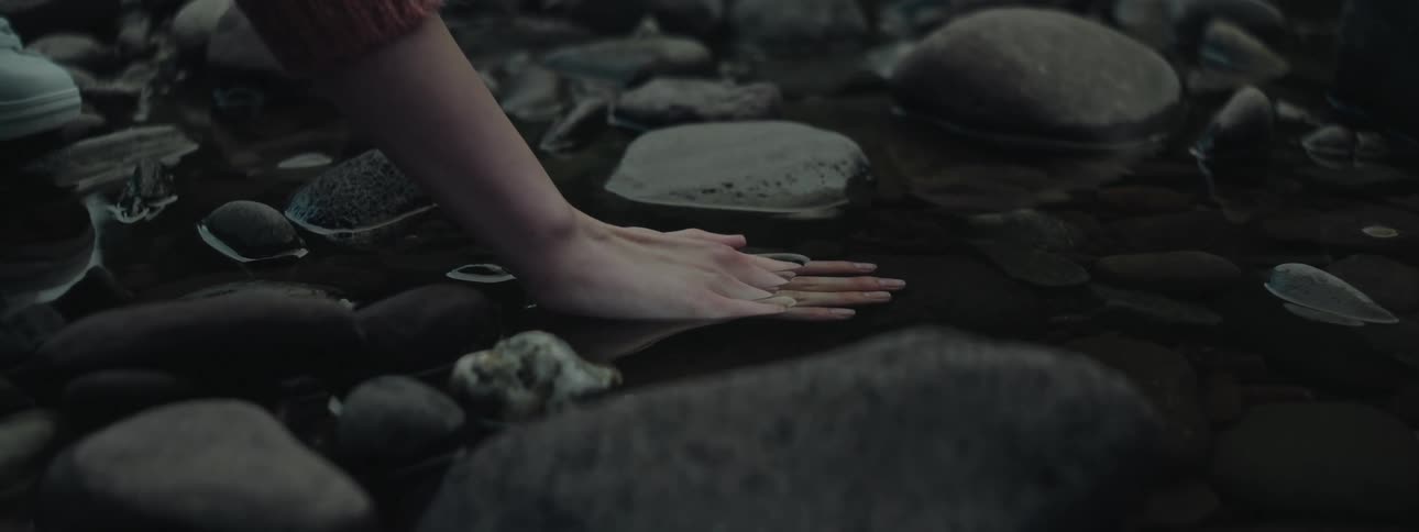 A persons hand with the palm in a puddle of water full of round pebbles
