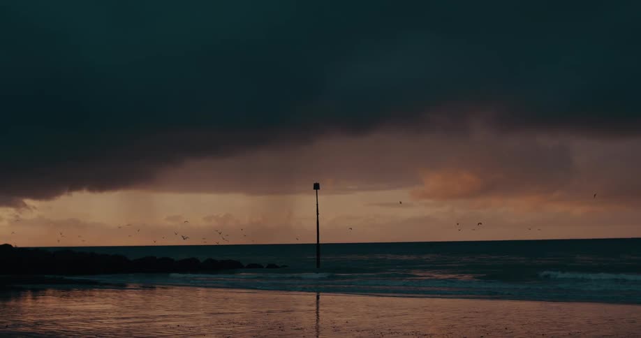 A dark storm cloud looming over the ocean with a lone post stands tall on the beach