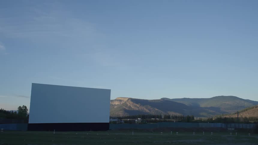 A large screen and lot at a drive in movie theater near mountains