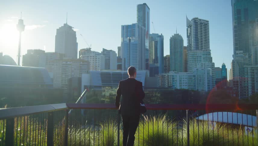 A man in a suit stands looking out over a large city skyline