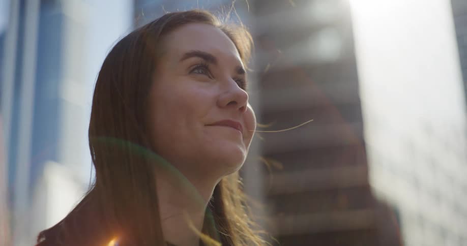 Woman standing downtown on a windy day smiles while looking around
