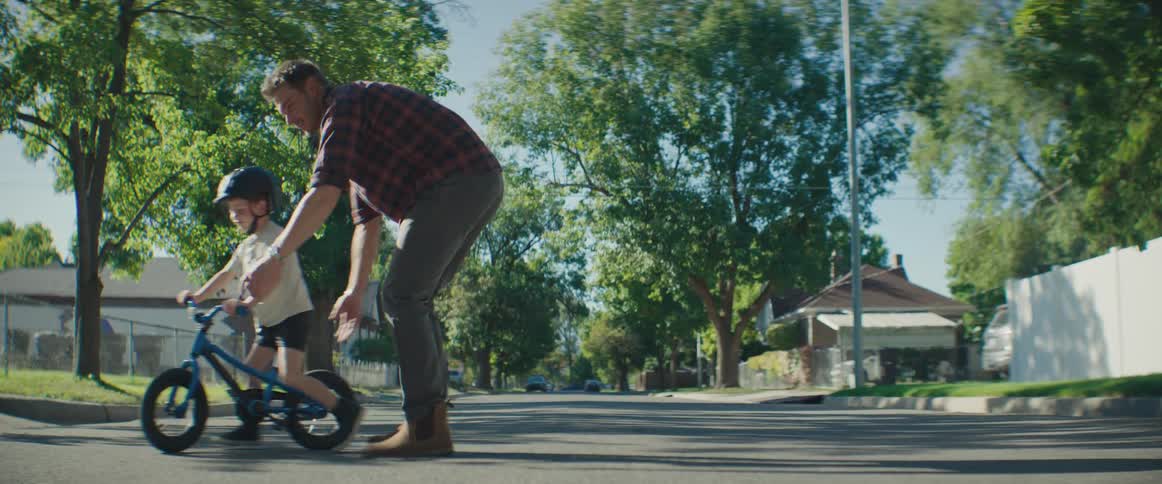Father teaching his young son to ride a bike on the street of a residential neighborhood
