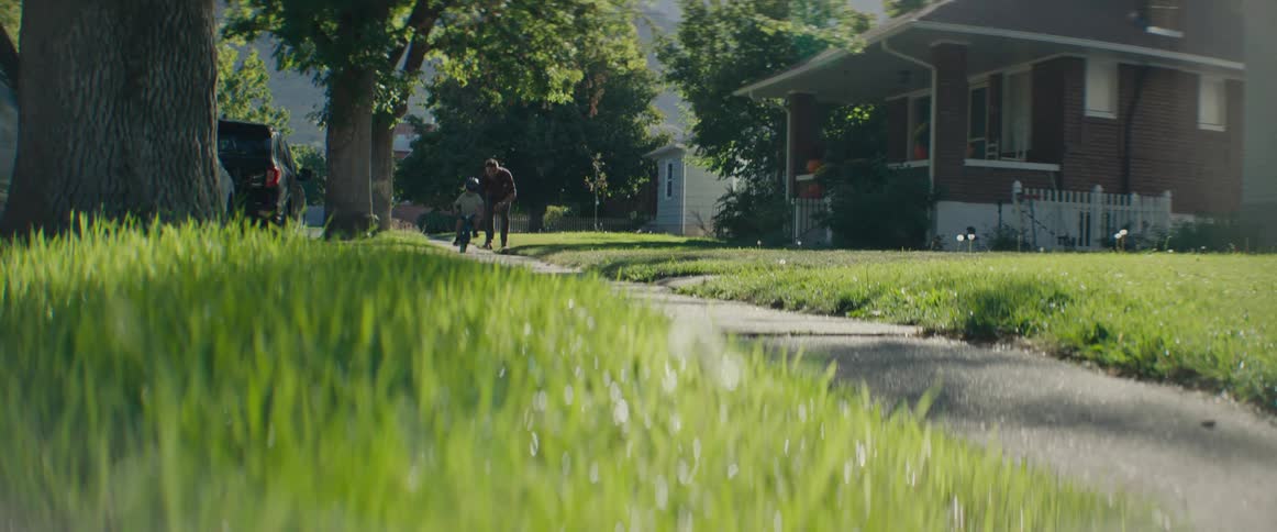 Father running on the sidewalk of a residential neighborhood with his young son riding a bike