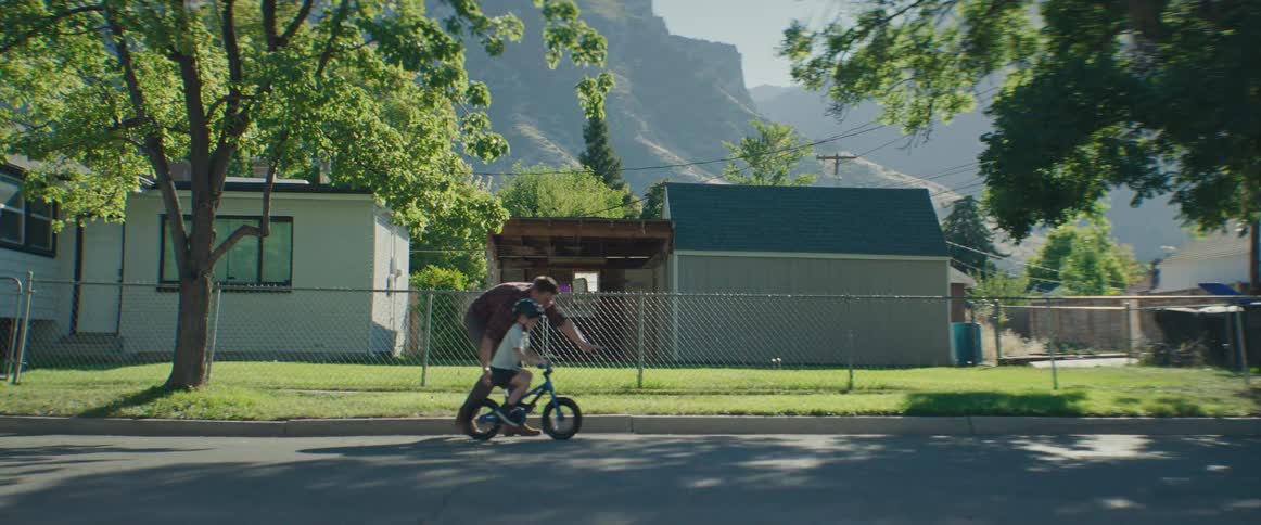 A father pushes his son along on a bicycle