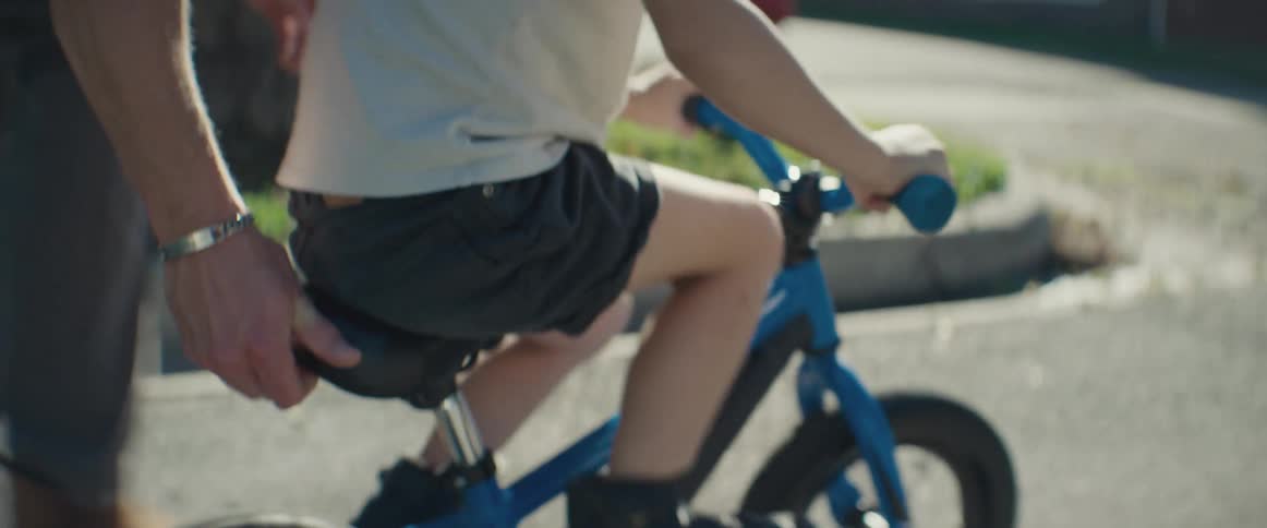 Hand of an adult helping and supporting a child learning how to ride a bike