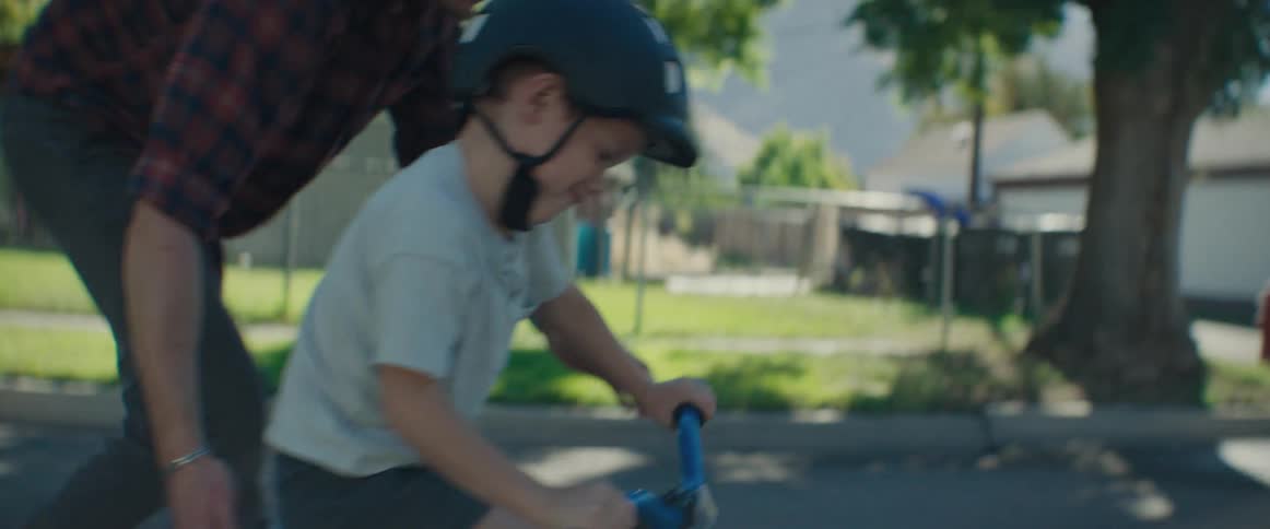 A father helps his son learn how to ride a bike on a suburban street