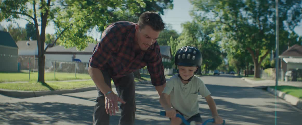 Father helps his child learn to ride a bike on a residential street