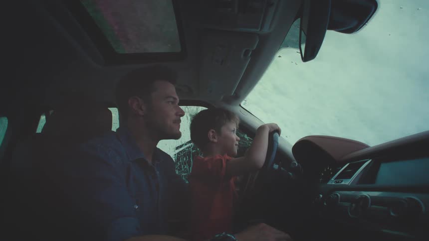 Father lets his son sit behind the wheel while their car passes through an automatic car wash