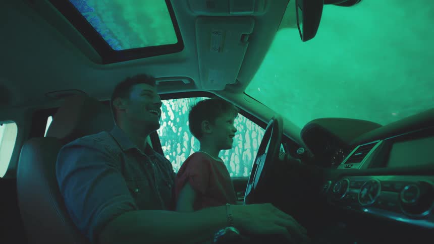 Father and son inside a car as the vehicle passes through a machine that washes the car with soap