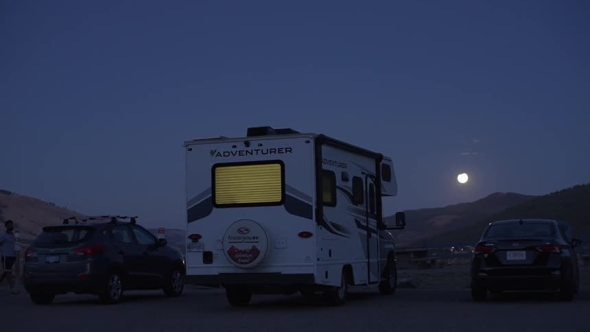 Motorhome and two cars parked in a field with mountains in the background at night