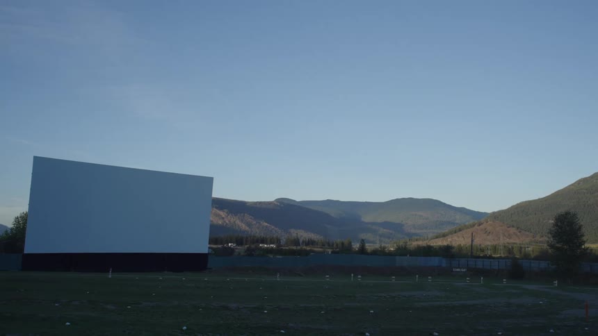 A large white drivein movie screen set against a backdrop of rolling hills and a clear blue sky