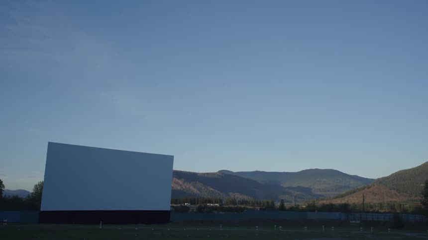 A large movie screen stands in a field for outdoor drivein theater
