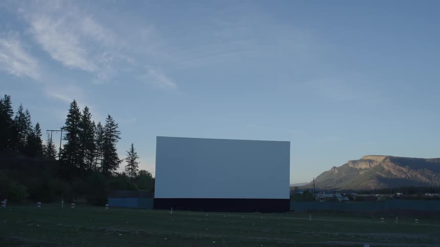 An outdoor screen at a drive in movie theater with traffic driving past nearby