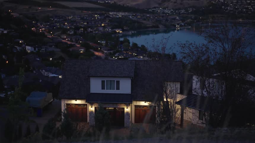 A suburban house on top of a hill overlooking a lake and a town