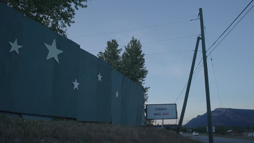 Fence with stars and a sign in the background next to a highway with vehicle traffic