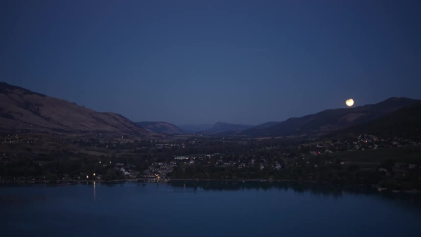 A coastal rural town sits in a large mountain valley underneath a night time moon