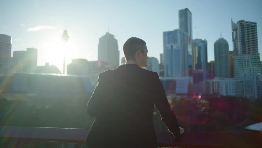 Man with black blazer walking from behind and looking out over a landscape of skyscrapers in a metropolis