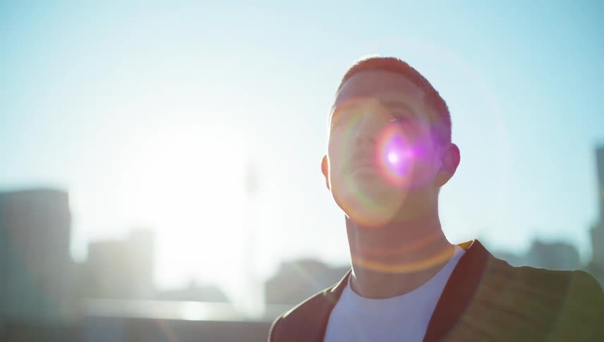 A man in a jacket looks up at the sky with a cityscape in the background