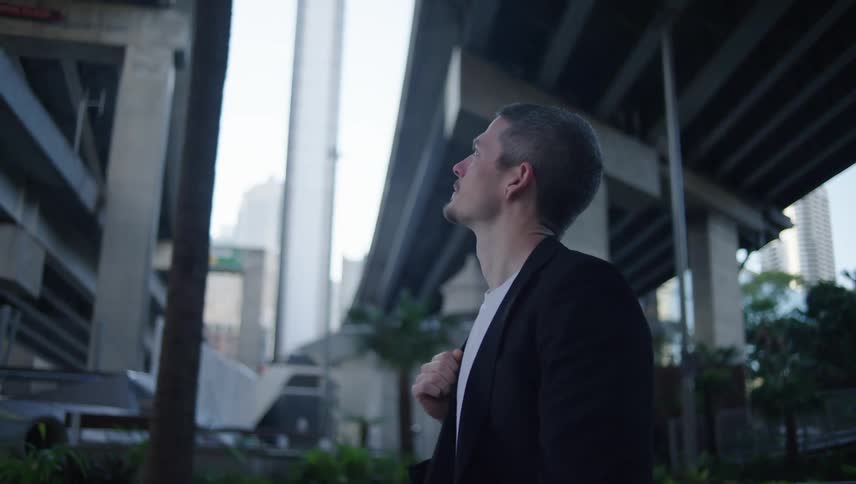 Man with black blazer and bag walking under an overpass in a metropolis