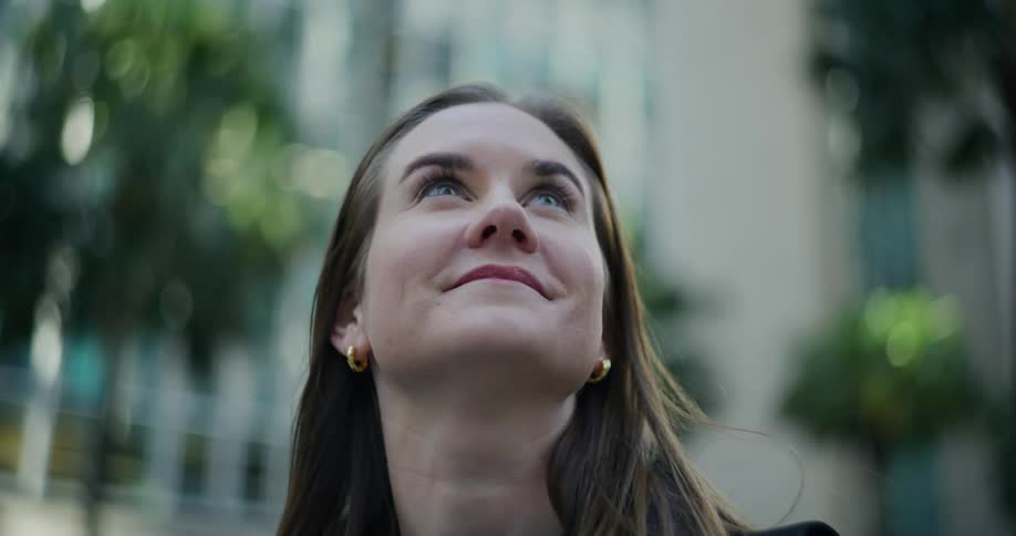 A womans face is being orbited around while she looks up at palm trees in awe