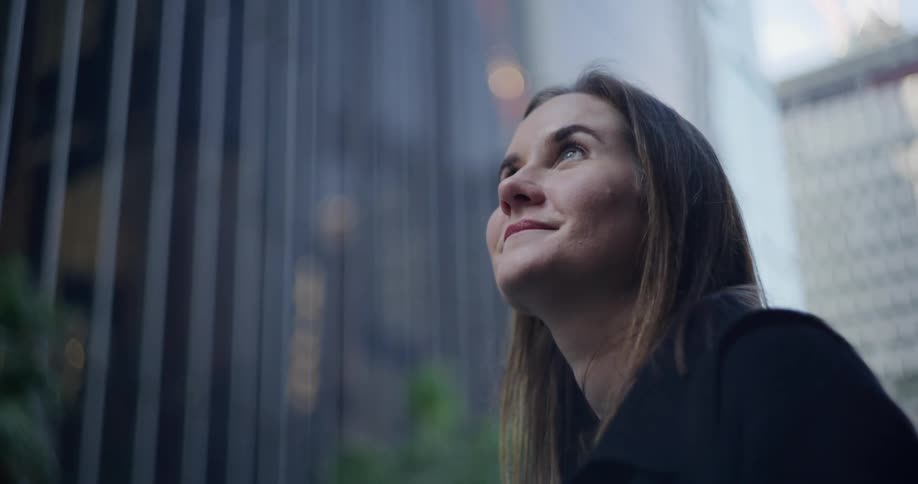 Woman with happy facial expression looking up while observing large buildings in a metropolis