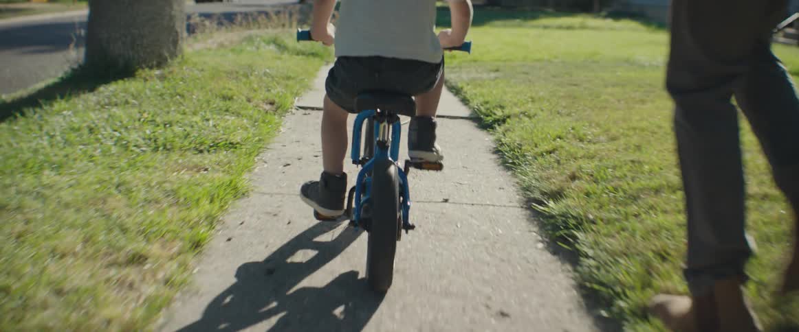 Father walking on the sidewalk with his son who is riding a bike during late afternoon