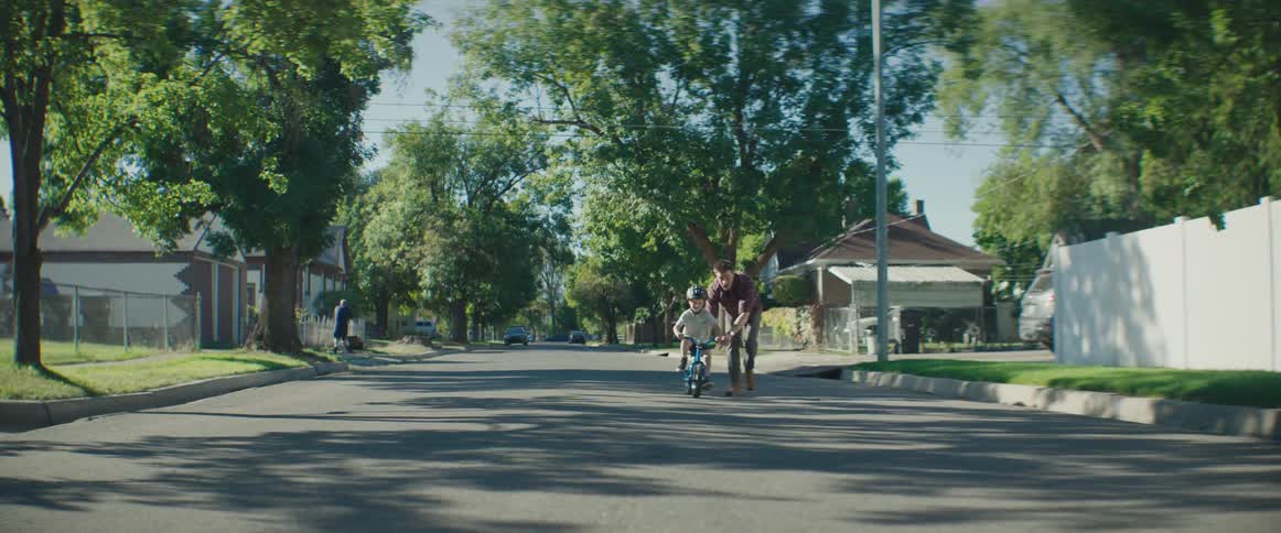 A father teaching his son to ride a bicycle on a suburban road