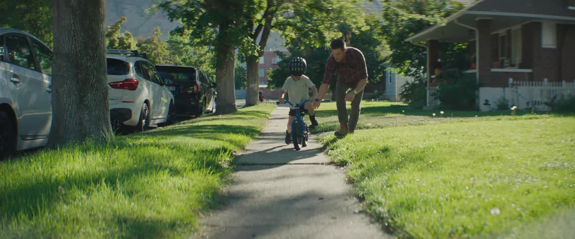 Father on the sidewalk of a residential neighborhood teaching his son to ride a bike