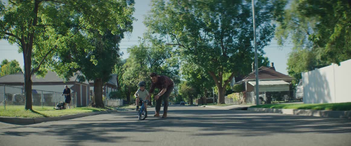 A man on a suburban road helping his son learn how to ride his bicycle