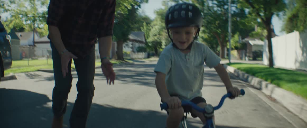 Father accompanying his young son to ride a bike on a street in a neighborhood