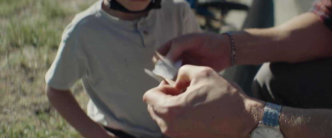 Father unwraps an bandage for his son who is wearing a bike helmet