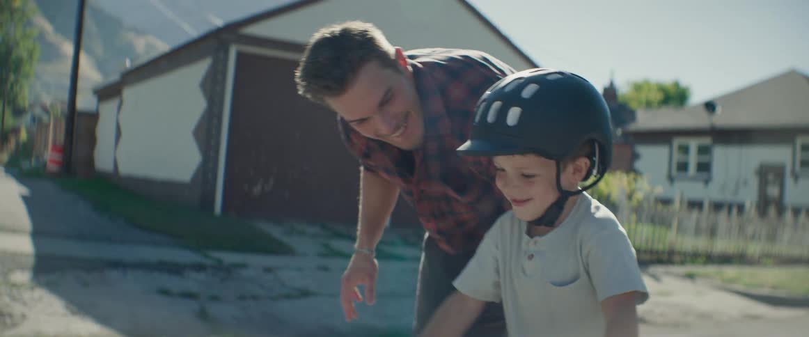Father teaches his son how to ride a bicycle in their residential neighborhood on a sunny day