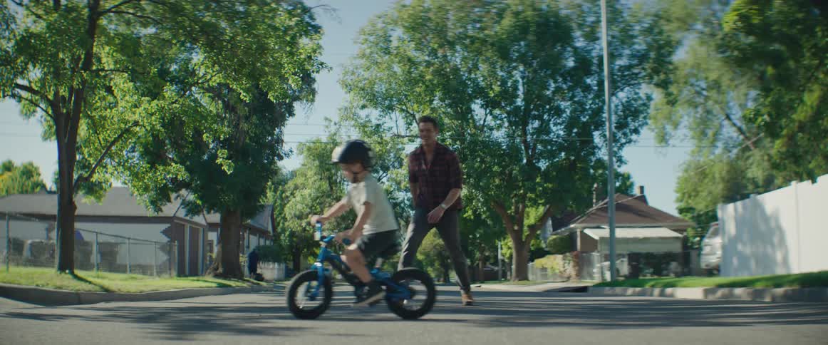 A father teaches his son to ride a bike on a suburban street in the summer