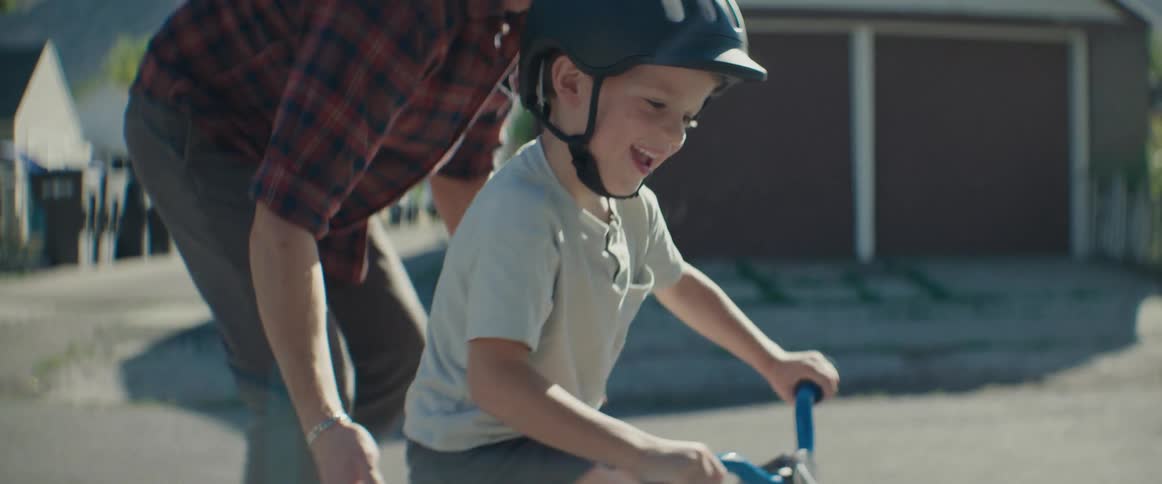 Adult person helping a boy ride a bike on the street
