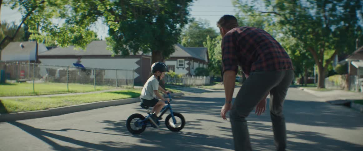 A father supports his son as he practices riding a bicycle without training wheels