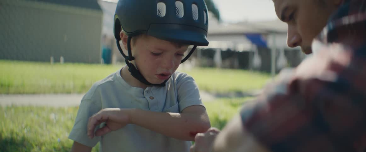 A father applies a bandage to his sons elbow after he fell off his bike