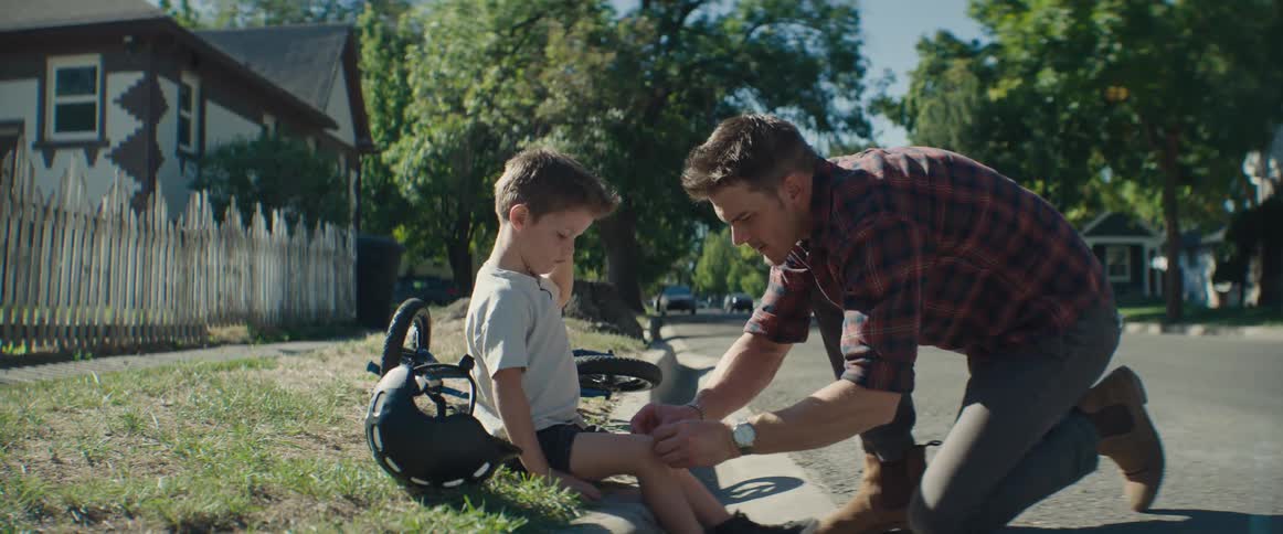 A father applies an adhesive bandage to his sons knee after the boy fell off his bicycle in the neighborhood