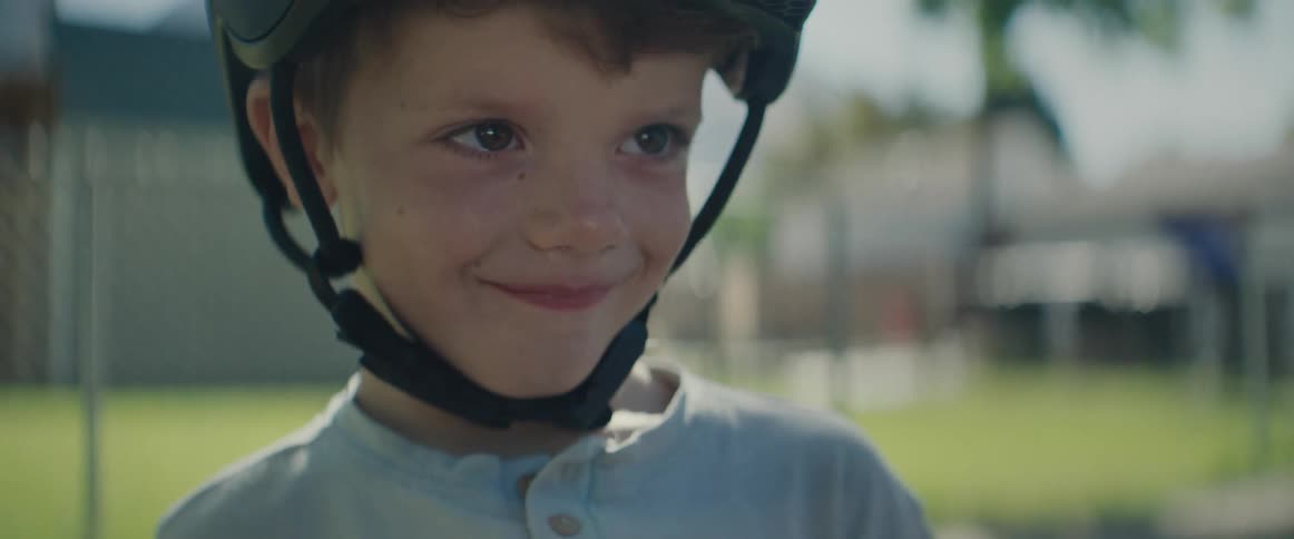 A young boy wearing a bike helmet gives a happy and mischevious smile