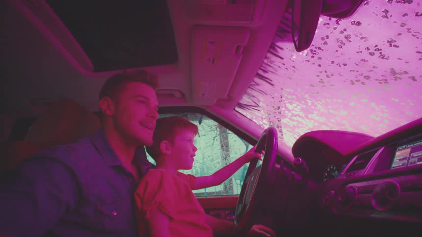 A father lets his son drive through a car wash