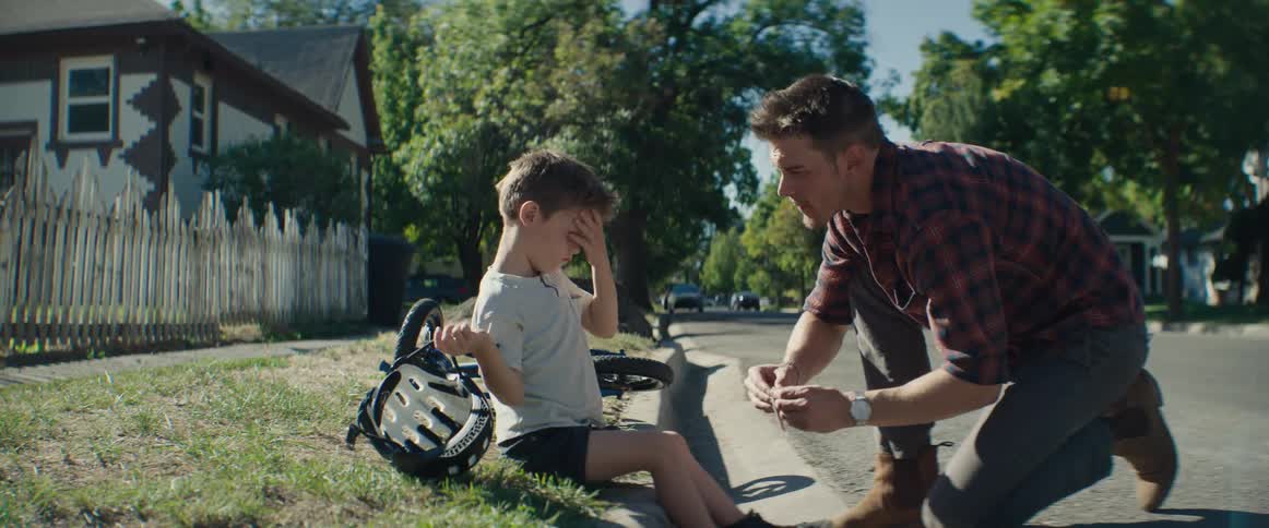 A father kneels down to comfort his son after he fell off his bike